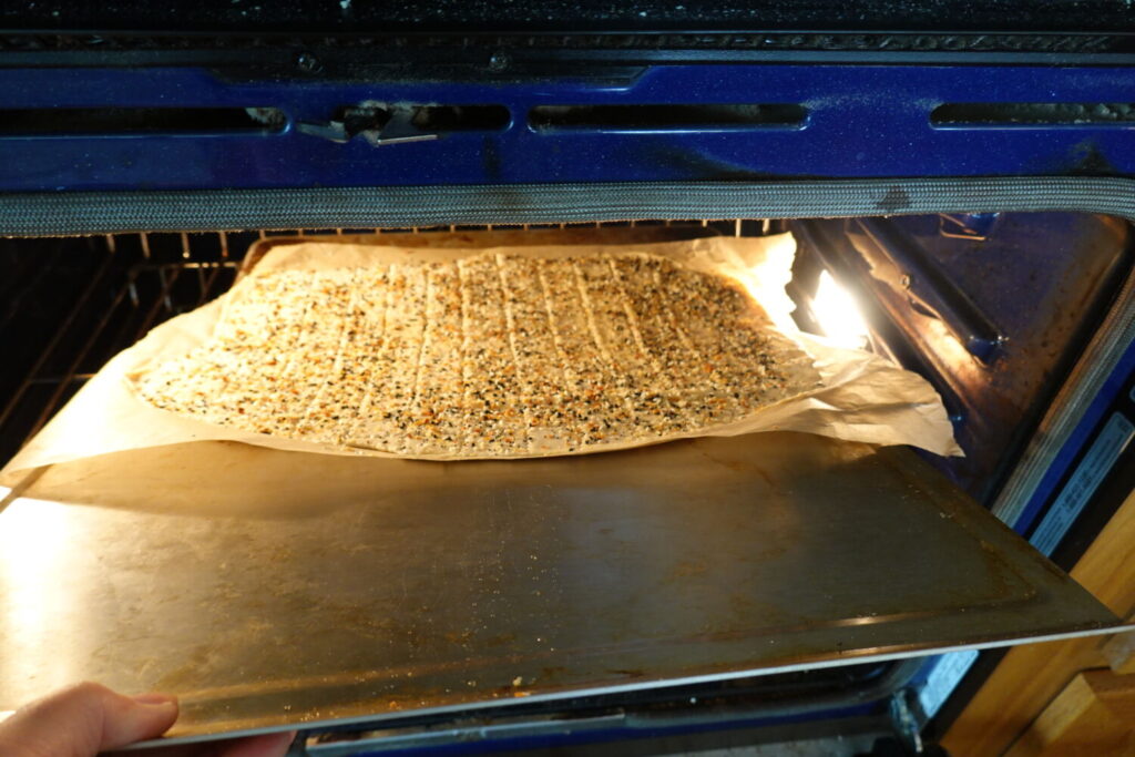 Rolled and cut sourdough everything crackers dough on parchment then moved from cool cookie sheet sliding onto hot cookie sheet preheated in the oven.